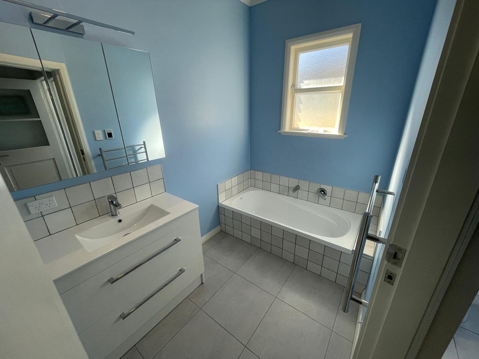 Blue-painted bathroom with white vanity, mirror cabinet, tiled-surround bath and chrome heated towel rail