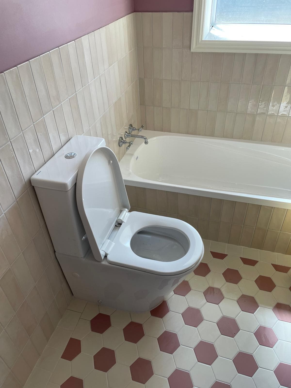 New toilet and bath with chrome wall-mounted taps, cream subway wall tiles and a pink and cream hexagon tiled floor