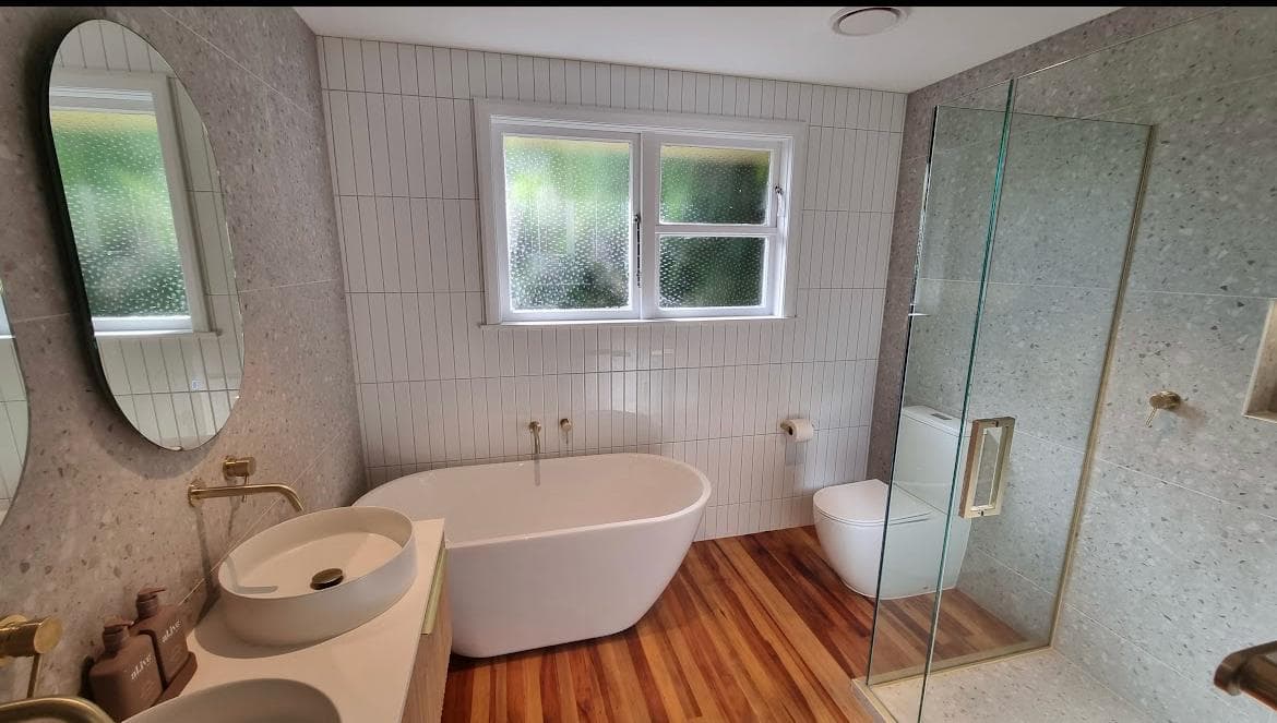 Freestanding bath with brass wall-mounted filler between a terrazzo feature wall, white tiled wall and timber floor