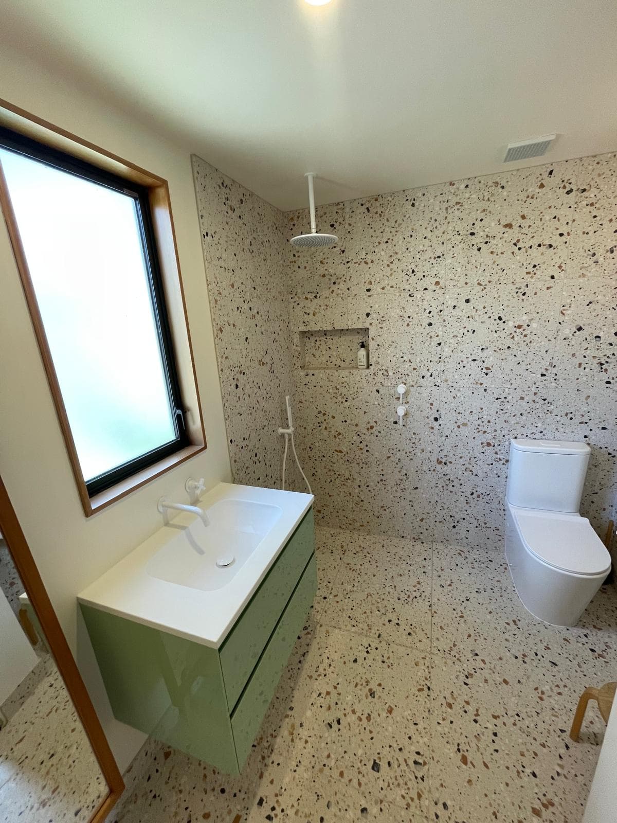 Walk-in tiled shower with ceiling-mounted rain head, recessed niche and sage green vanity in a terrazzo-tiled bathroom