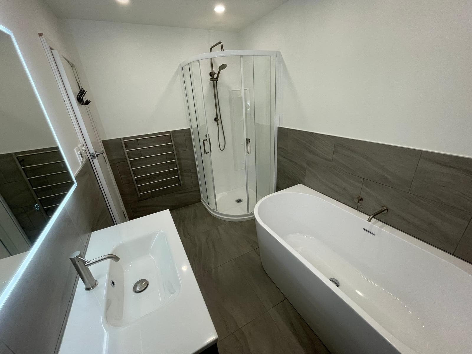Corner shower unit, freestanding bath and heated towel rail in a renovated grey and white bathroom