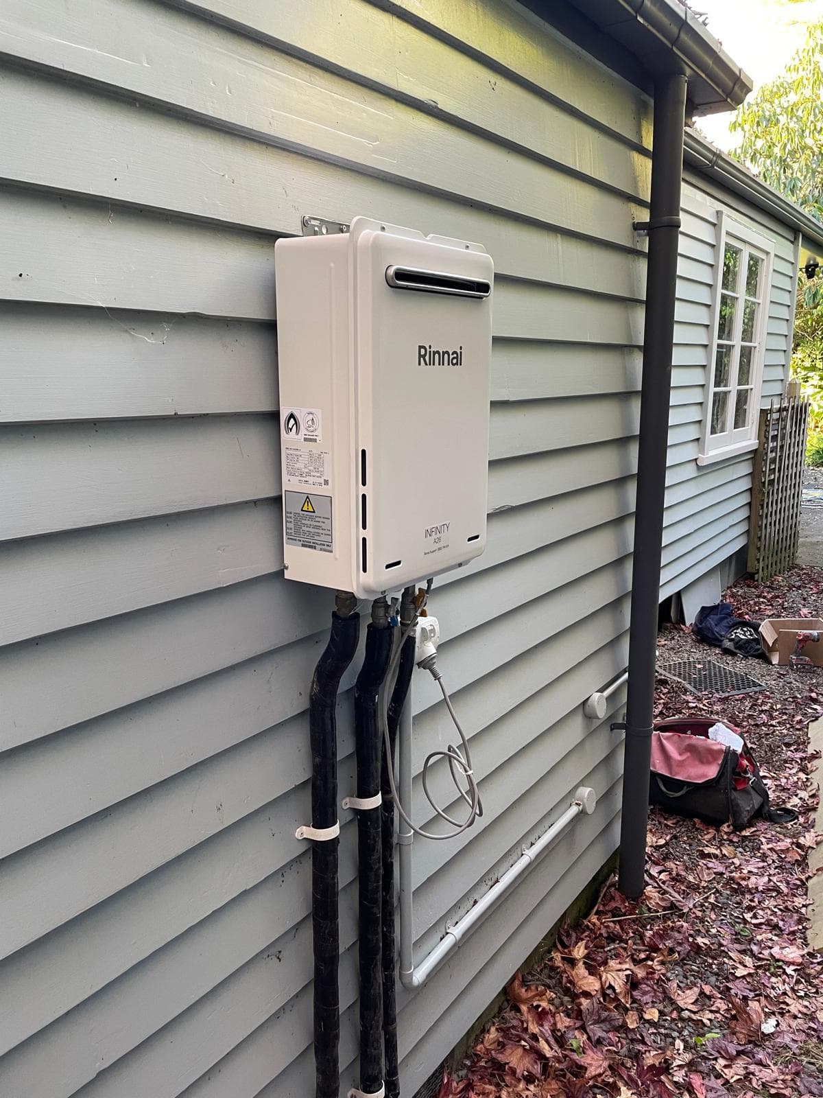 Rinnai Infinity A26 continuous-flow gas water heater installed on the weatherboard wall of a villa