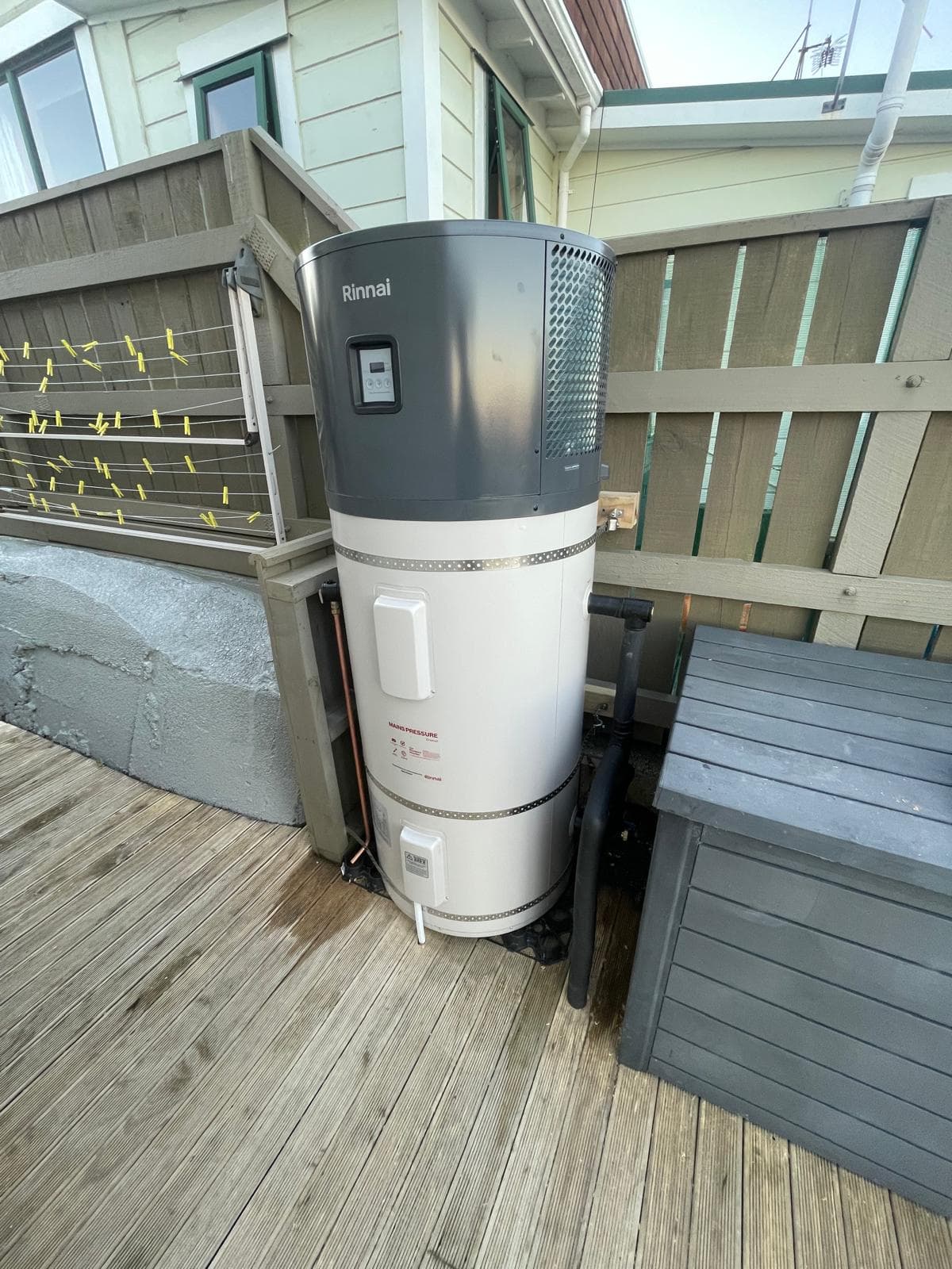 Rinnai hot water heat pump cylinder installed on a timber deck beside a house